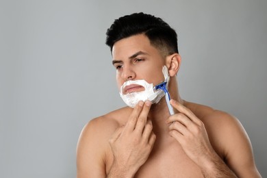 Photo of Handsome man shaving with razor on grey background