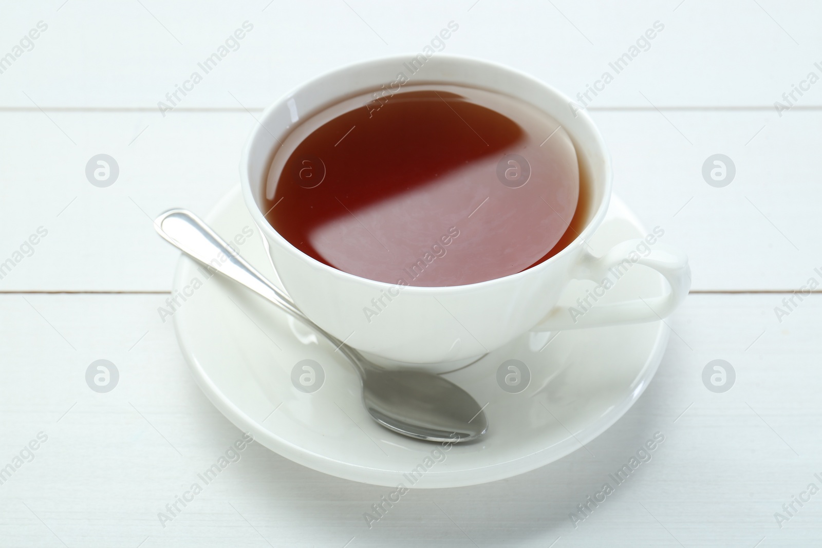 Photo of Aromatic tea in cup and spoon on white wooden table