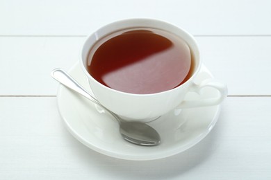 Photo of Aromatic tea in cup and spoon on white wooden table