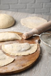 Photo of Raw chebureki with tasty filling and rolling pin on wooden table