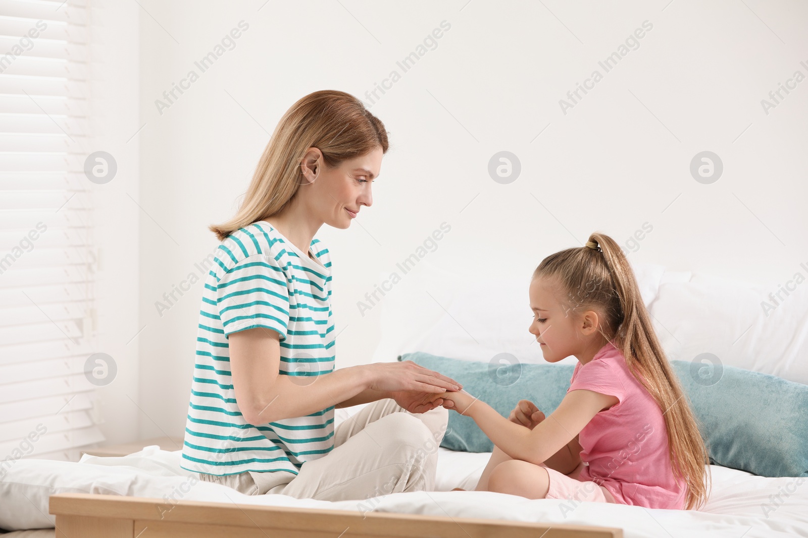 Photo of Mother applying ointment onto her daughter's hand on bed at home