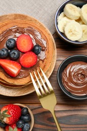 Photo of Tasty pancakes with chocolate paste, berries and banana served on wooden table, flat lay