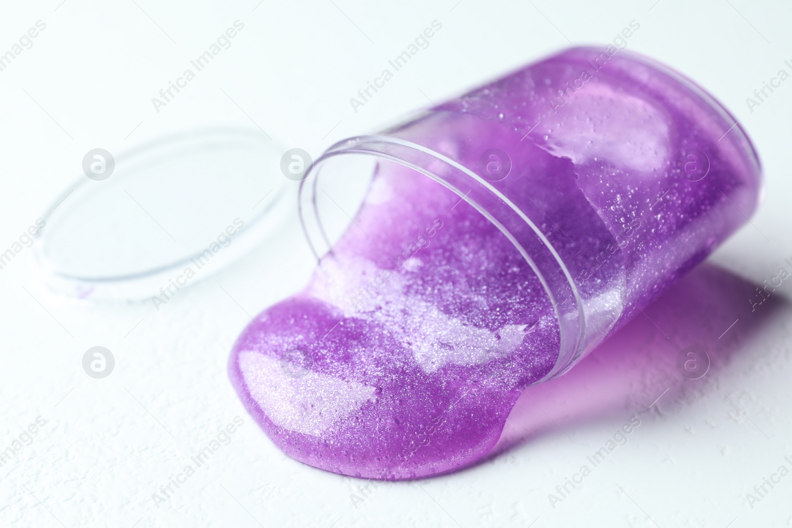 Photo of Overturned plastic container with purple slime on white background, closeup