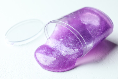 Photo of Overturned plastic container with purple slime on white background, closeup