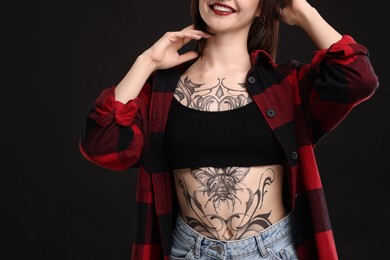 Photo of Smiling woman with cool tattoos on black background, closeup
