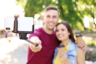 Photo of Young couple taking selfie with monopod outdoors, focus on smartphone