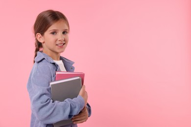 Photo of Portrait of smiling schoolgirl with books on pink background. Space for text