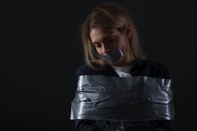 Photo of Woman taped up and taken hostage on dark background. Space for text