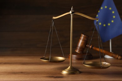 Photo of Scales of justice, judge's gavel and European Union flag on wooden table. Space for text