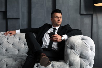 Handsome businessman with smartphone on sofa indoors. Luxury lifestyle