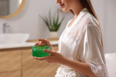 Young woman holding jar of aloe gel indoors, closeup