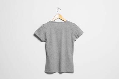 Photo of Hanger with grey t-shirt on light wall. Mockup for design