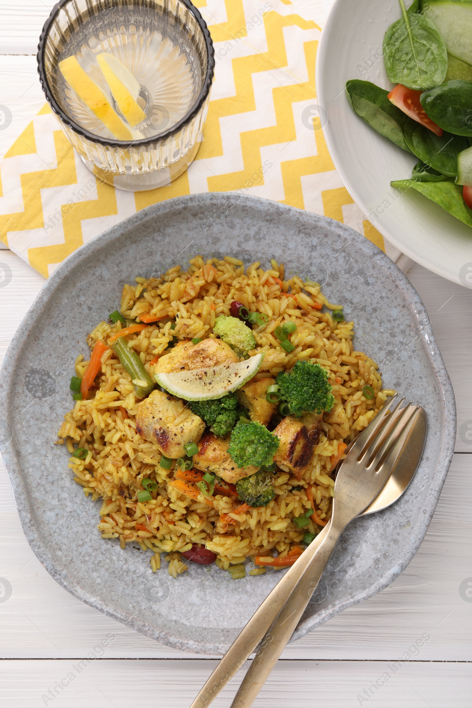 Photo of Tasty rice with meat and vegetables in plate served on white wooden table, flat lay