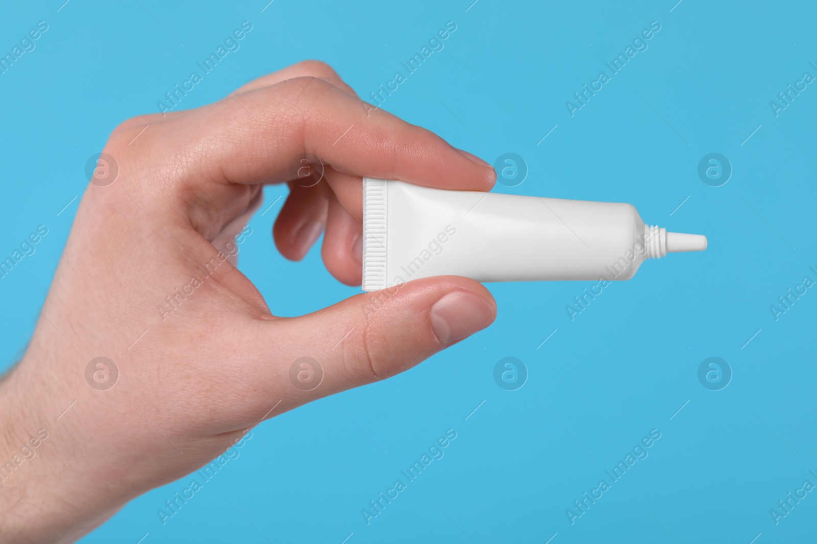 Photo of Man holding tube of ointment on light blue background, closeup