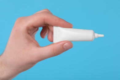 Man holding tube of ointment on light blue background, closeup