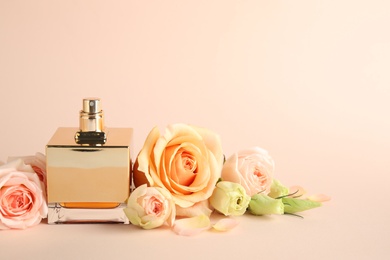 Photo of Bottle of perfume with fresh flowers on beige background, space for text