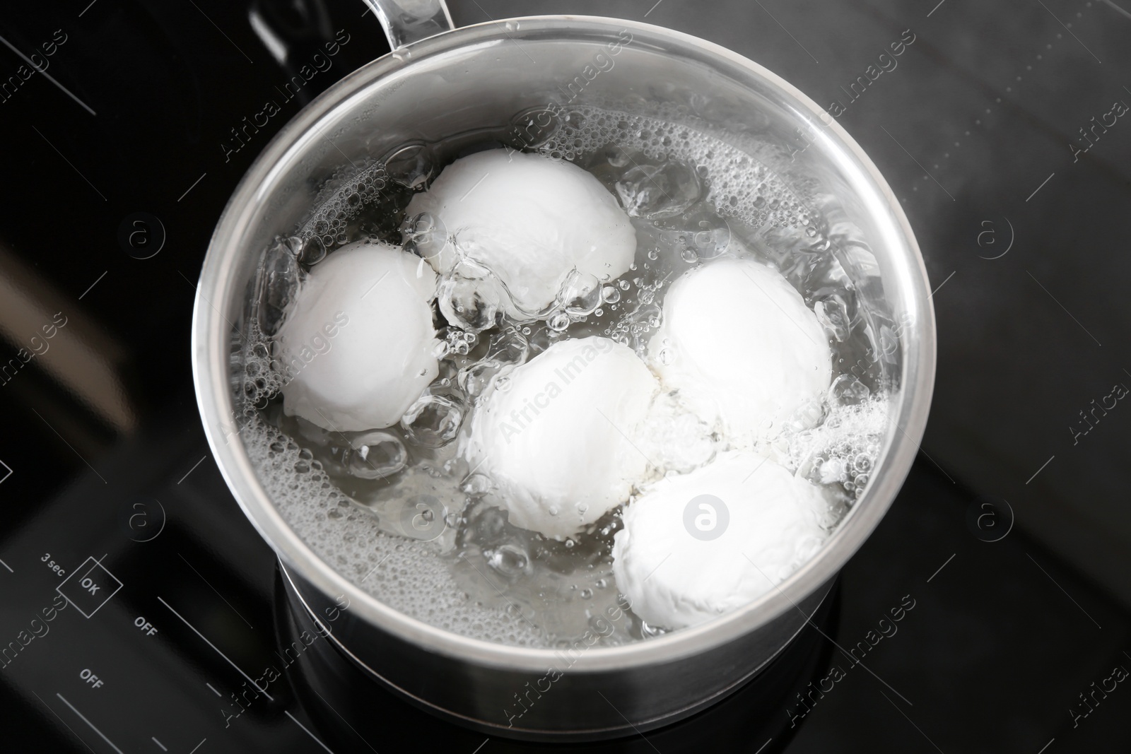 Photo of Chicken eggs boiling in saucepan on electric stove, above view