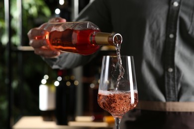 Photo of Man pouring rose wine from bottle into glass indoors, closeup