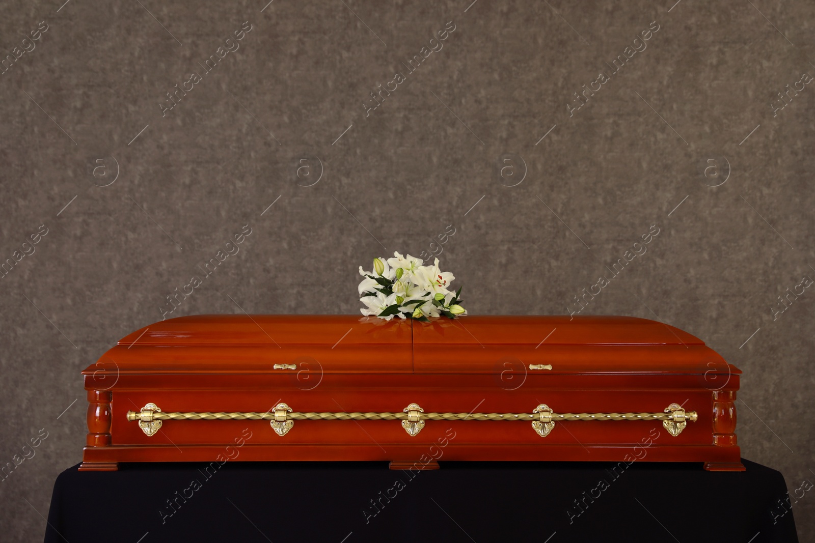 Photo of Wooden funeral casket with white lilies at grey wall