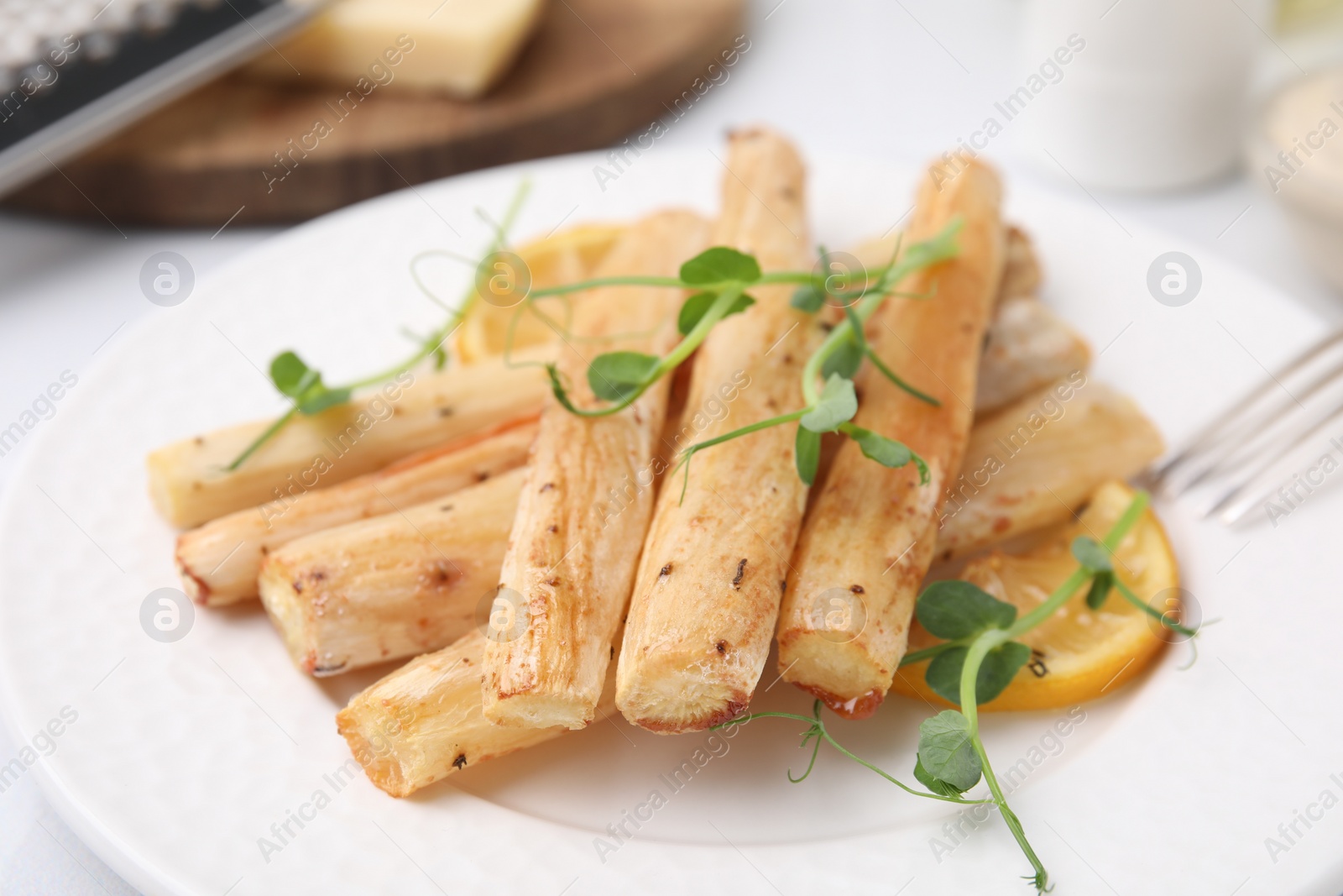 Photo of Plate with baked salsify roots and lemon on table, closeup