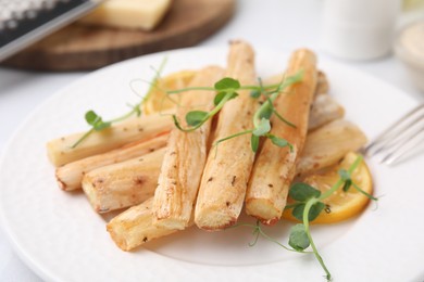 Plate with baked salsify roots and lemon on table, closeup