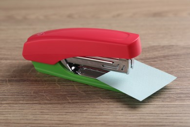 Photo of One new bright stapler with paper note on wooden table, closeup