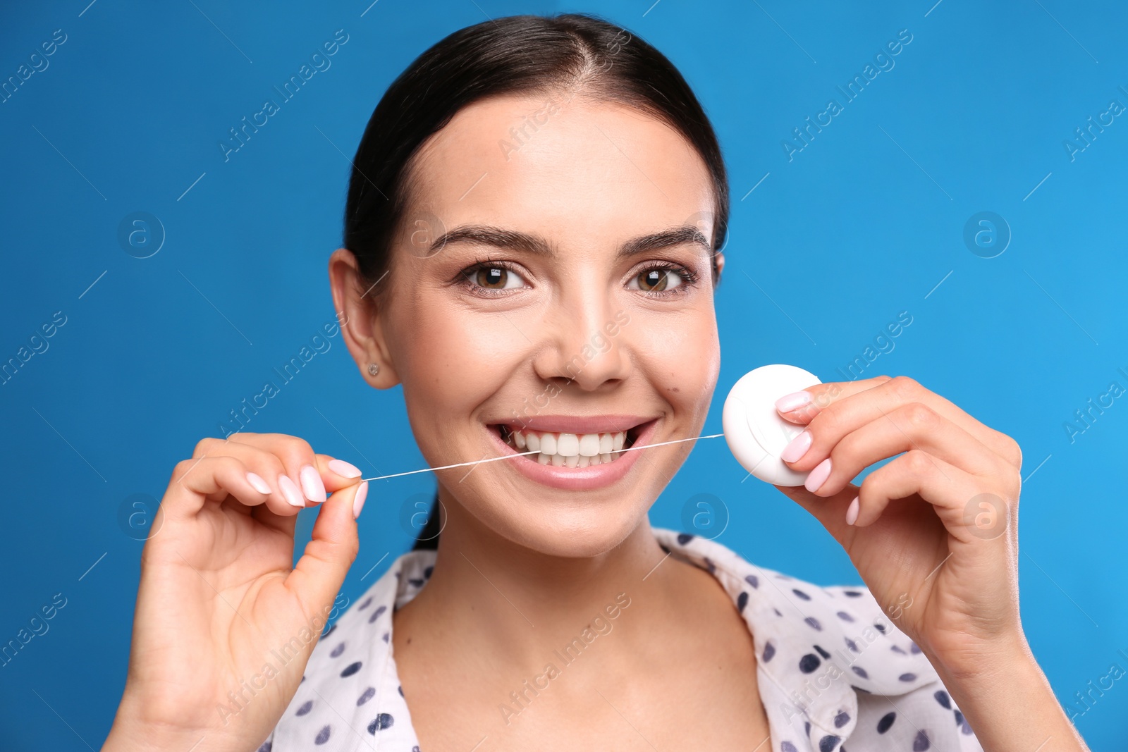 Photo of Young woman flossing her teeth on blue background. Cosmetic dentistry