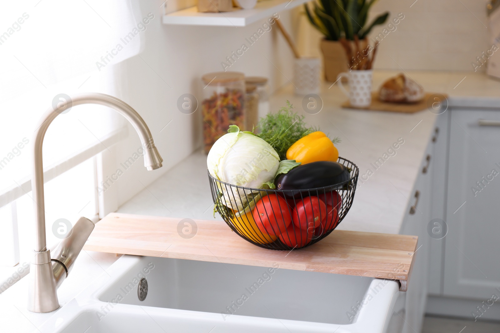 Photo of Basket full of different vegetables on wooden board in modern kitchen