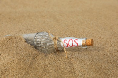 Photo of Glass bottle with SOS message on sand, closeup
