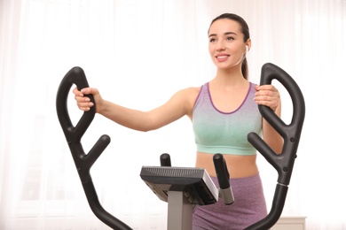 Photo of Young woman using modern elliptical machine indoors