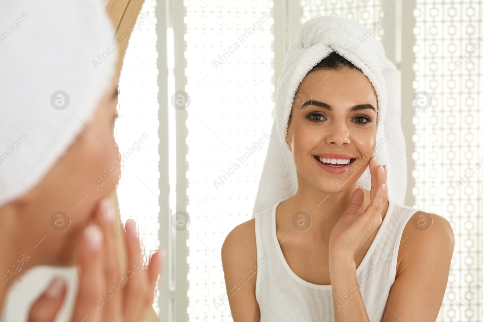 Photo of Happy young woman with clean skin looking at mirror in bathroom