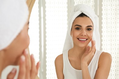 Happy young woman with clean skin looking at mirror in bathroom