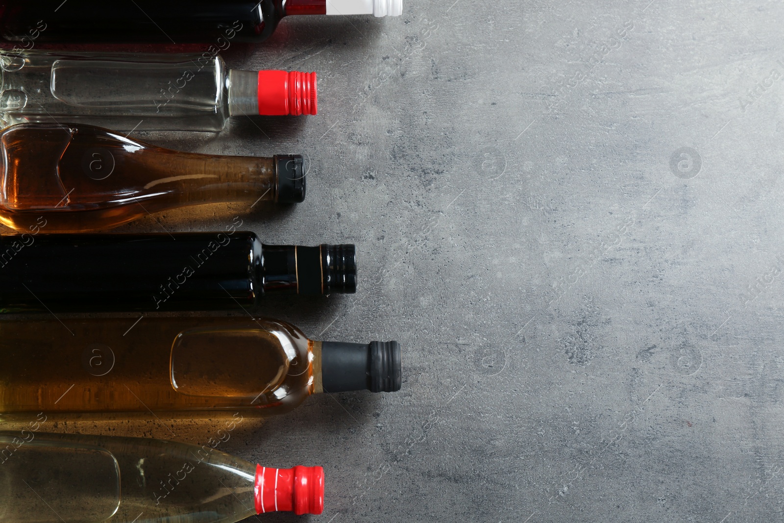 Photo of Bottles with different kinds of vinegar and space for text on grey background, flat lay