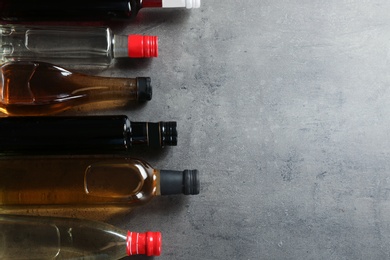 Photo of Bottles with different kinds of vinegar and space for text on grey background, flat lay