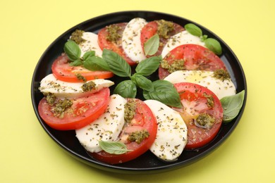 Photo of Plate of delicious Caprese salad with pesto sauce on yellow table, closeup