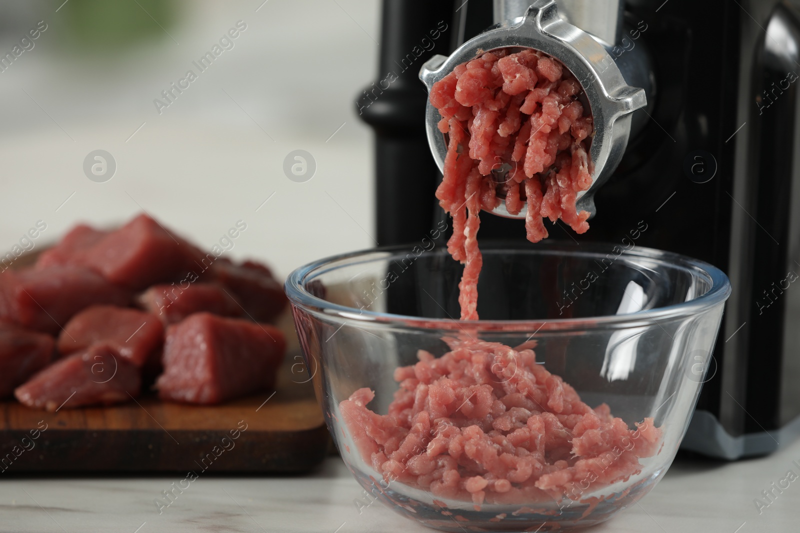 Photo of Electric meat grinder with beef mince on white table against blurred background, selective focus. Space for text