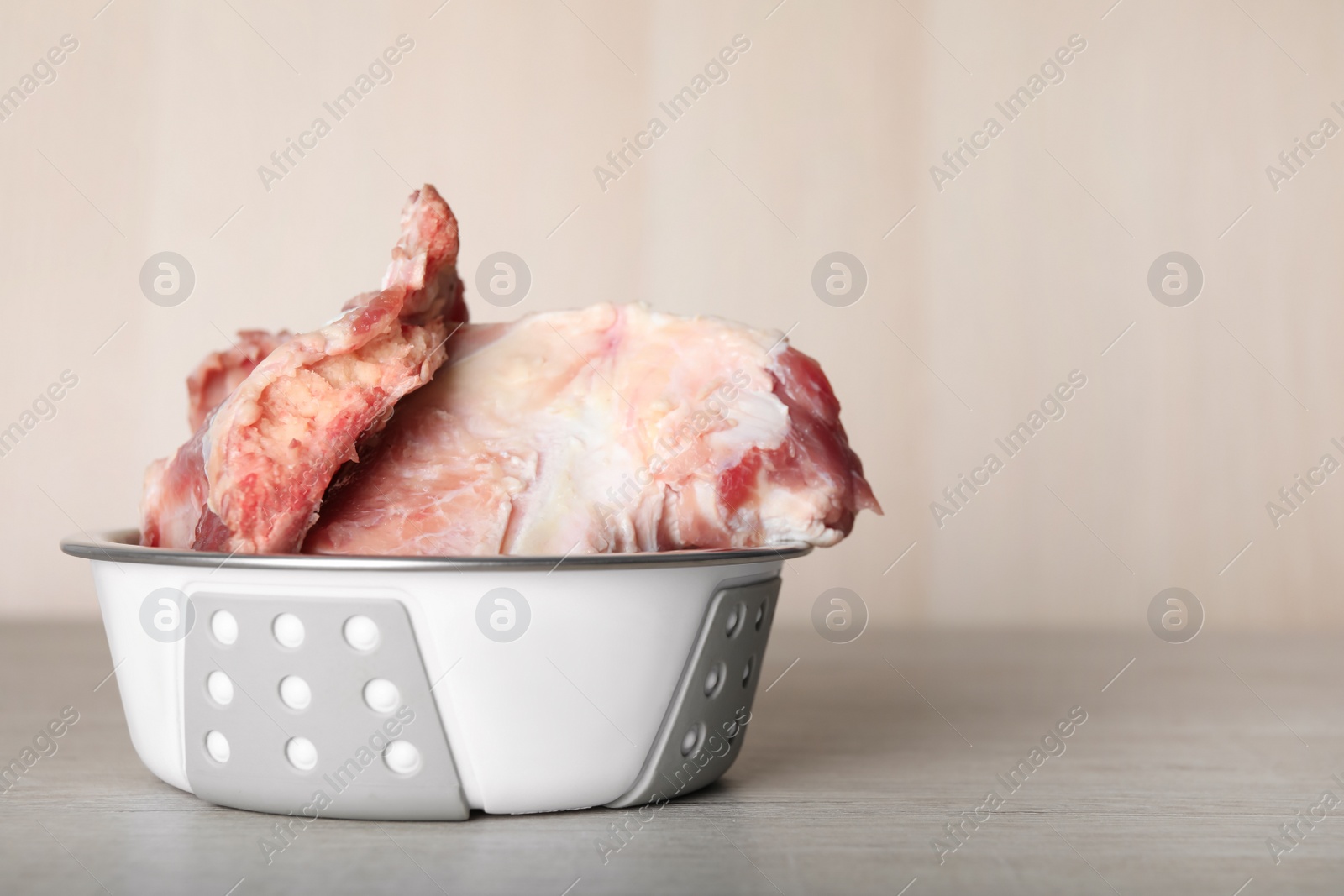 Photo of Feeding bowl with raw meaty bones on white wooden table. Space for text