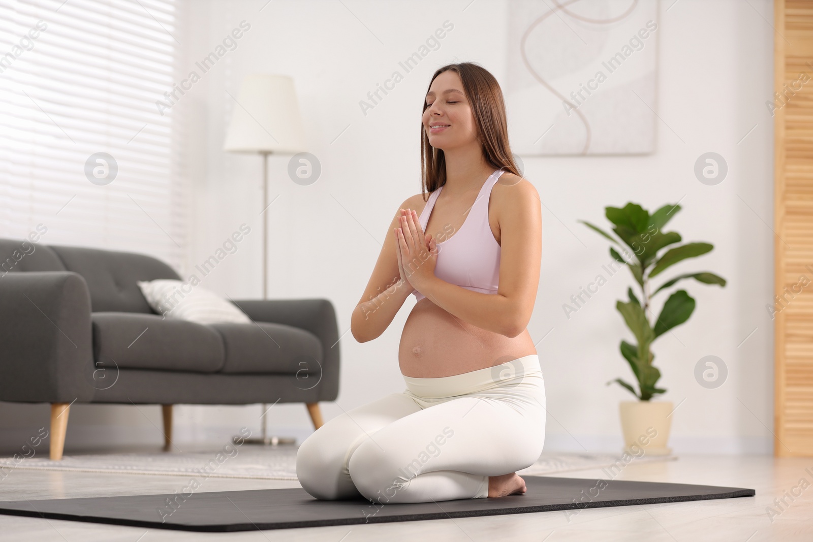 Photo of Pregnant woman meditating on yoga mat at home, space for text