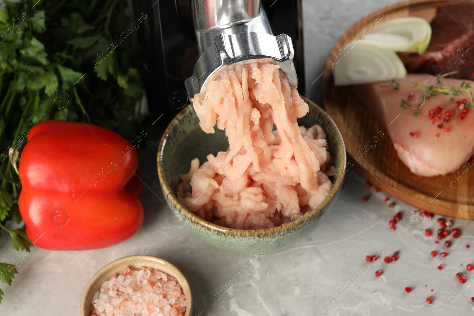 Photo of Electric meat grinder with chicken mince and products on grey marble table