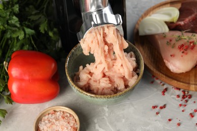 Electric meat grinder with chicken mince and products on grey marble table