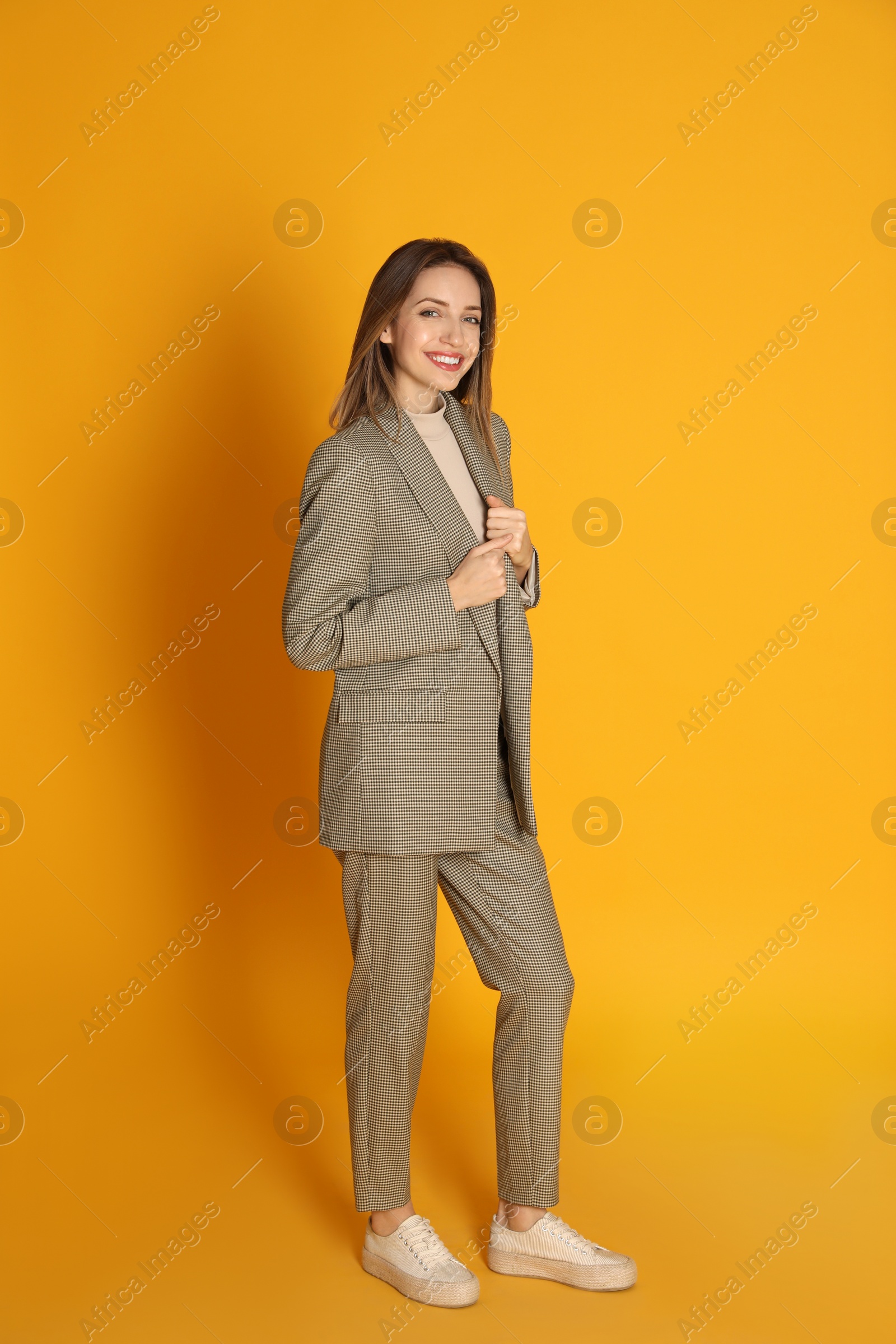 Photo of Full length portrait of beautiful young woman in fashionable suit on yellow background. Business attire