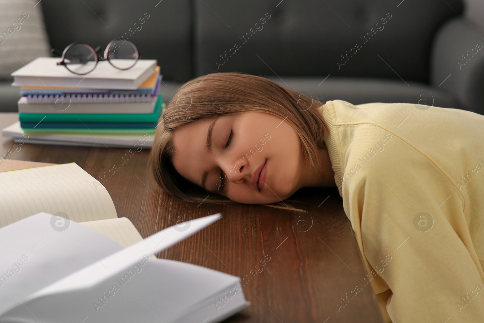 Photo of Young tired woman sleeping near books at wooden table indoors