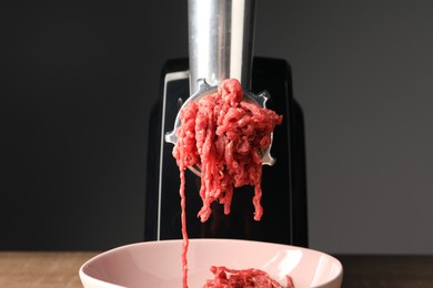Electric meat grinder with beef mince on table against grey background