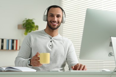 Photo of Young man with headphones working on computer at desk in room. Home office