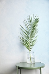 Photo of Vase with tropical date palm leaf on table near color wall