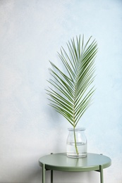 Vase with tropical date palm leaf on table near color wall