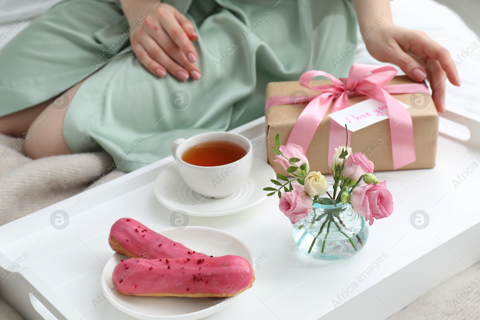 Photo of Tasty breakfast served in bed. Woman with gift box, tea, eclairs, flowers and I Love You card at home, closeup