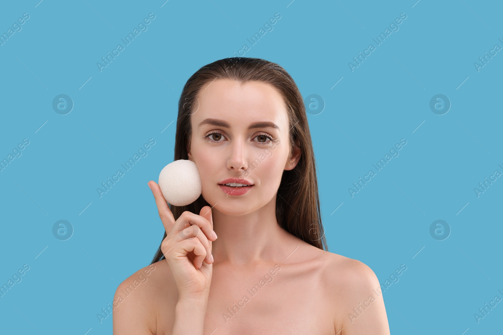 Photo of Young woman holding face sponge on light blue background