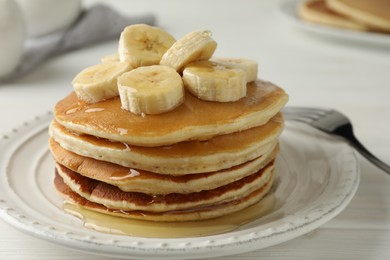 Photo of Delicious pancakes with bananas and honey on white wooden table, closeup