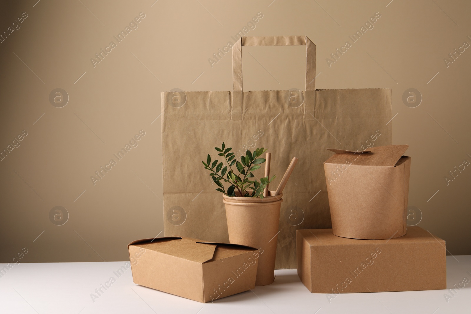 Photo of Eco friendly food packaging. Paper containers, bag, straws and green twigs on white table against beige background. Space for text